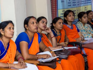 Line of women in saris listening to a presentation. They are India's accredited social health activists (ASHAs) being trained on the health issues caused by air pollution. Photo by Megha Namdeo